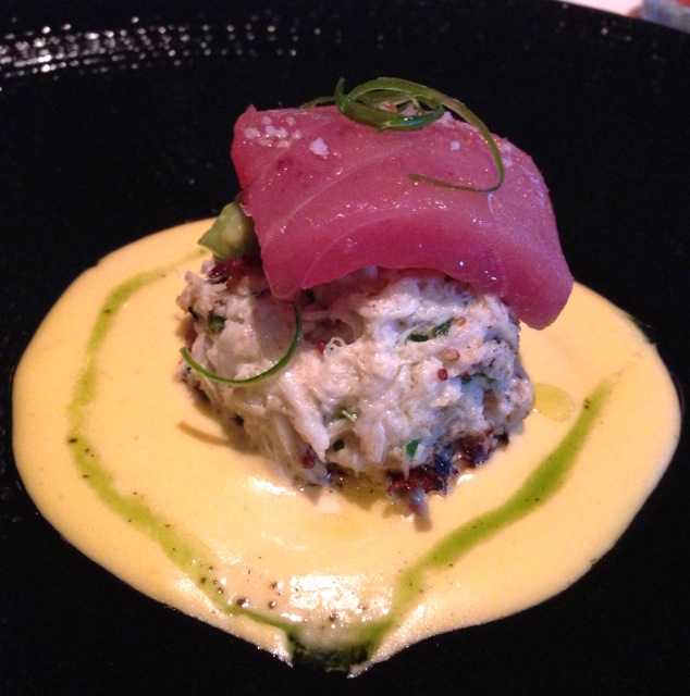 A seared crab cake sitting on a sweet corn puree with avocado relish, topped with ahi tuna and a sprinkle of sea salt